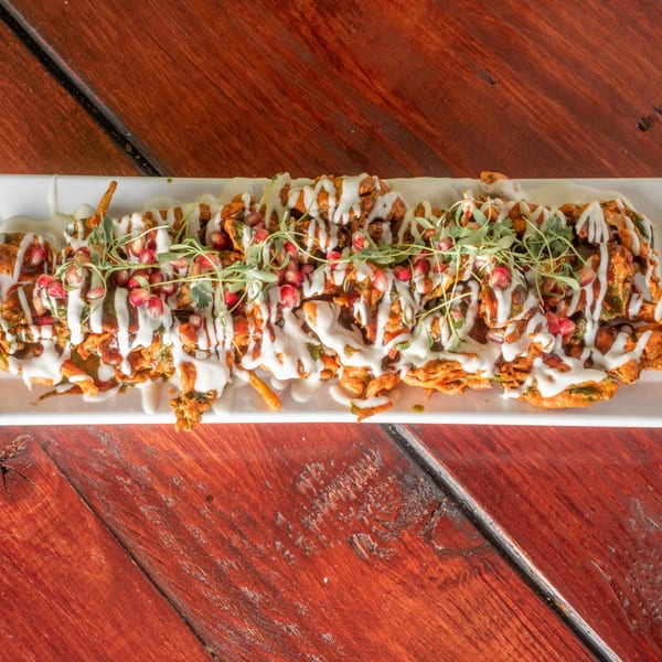 Indian pakora dish with white sauce, green herbs, and pomegranate seeds on a white platter.