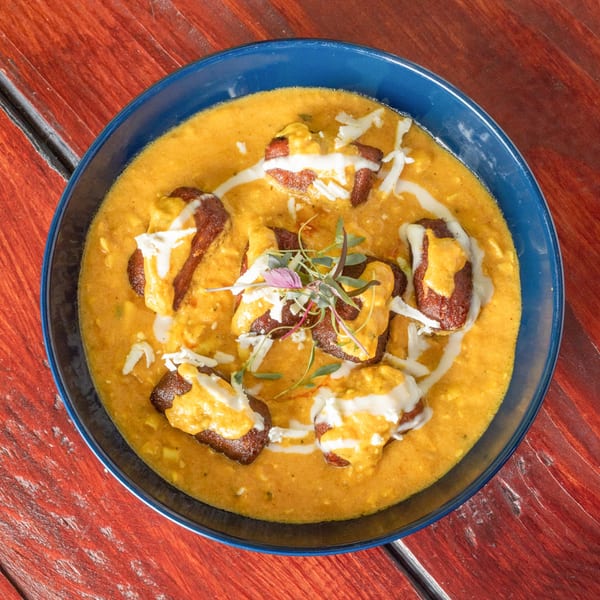 Indian dish with red pieces in a yellow sauce, drizzled with white cream and garnished with herbs.