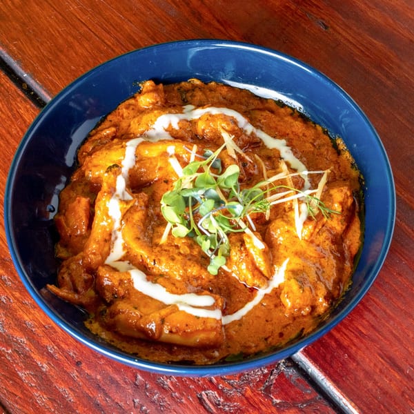 Indian butter chicken in a blue bowl, garnished with cream swirls, microgreens, and ginger slivers.