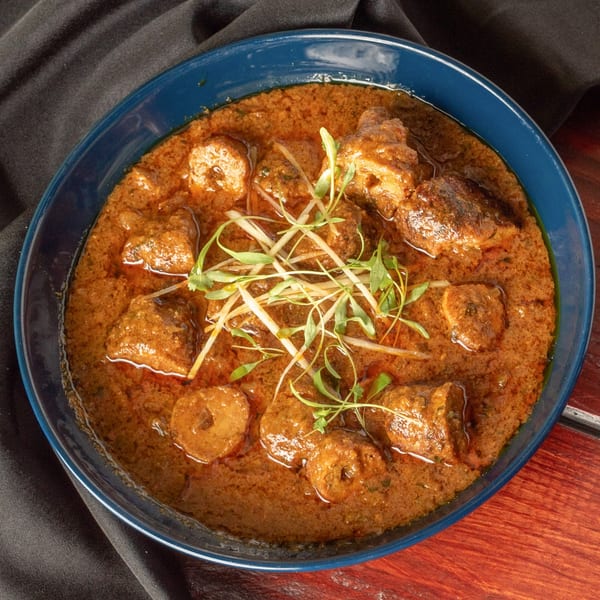 Indian curry with meat pieces and garnished with fresh herbs in a blue bowl.