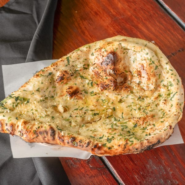 Garlic naan bread, topped with herbs and garlic, on a wooden table with a dark napkin.