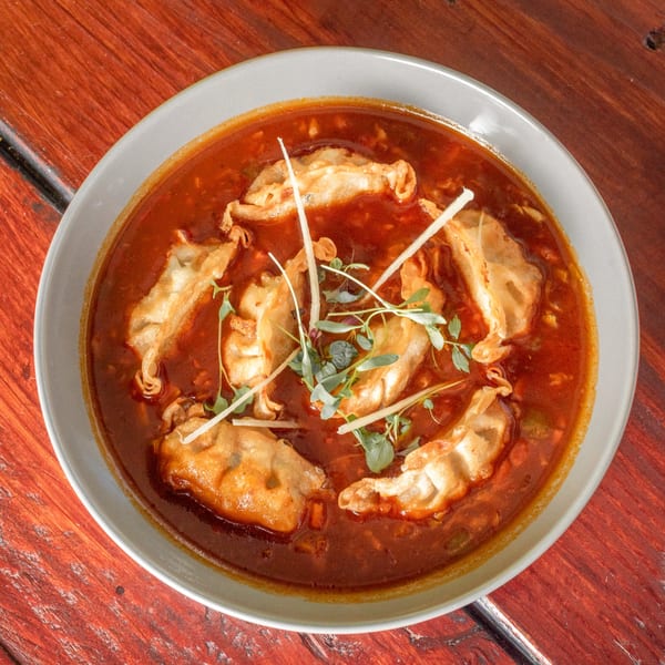 A bowl of Indian momo dumplings in a rich red sauce, garnished with herbs and ginger.