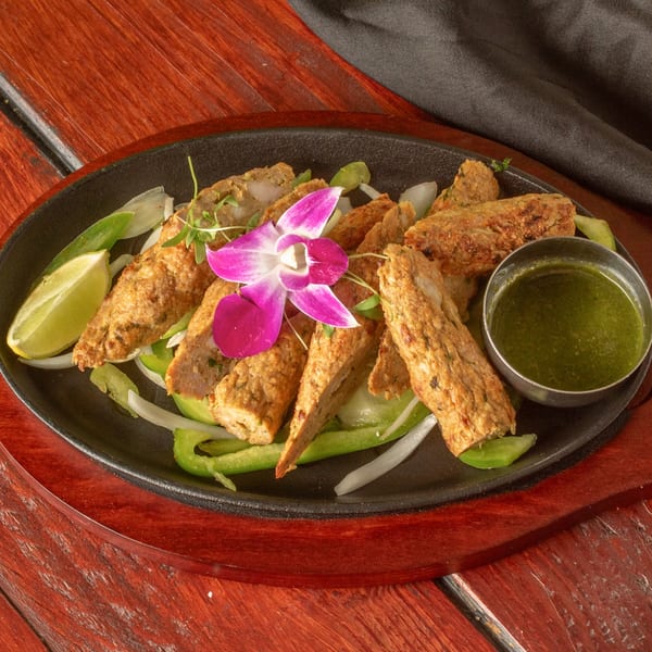 Indian seekh kebabs with green peppers, onions, lime, and green chutney, garnished with an orchid.