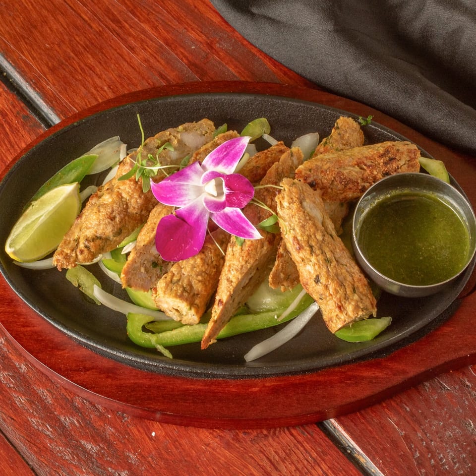 Indian seekh kebabs with green peppers, onions, lime, and green chutney, garnished with an orchid.