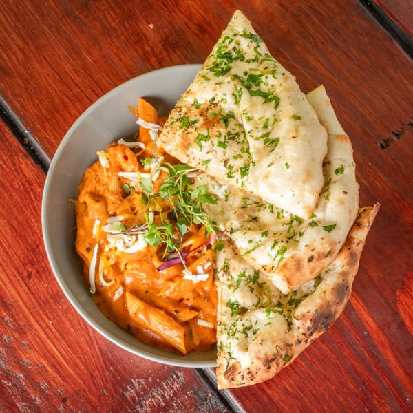 Indian fusion pasta with creamy orange sauce, topped with microgreens and shredded cheese, served with naan.
